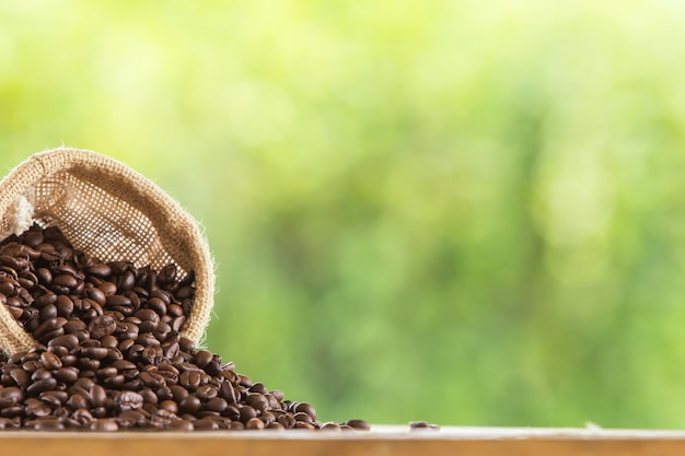 Coffee bean in sack on wooden  tabletop against grunge green blur background