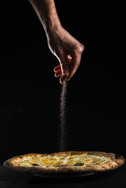 Crop hand pouring spices on pizza