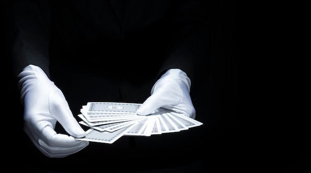 Magician's hand selecting card from fanned deck of playing card against black background