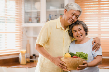 Asian elderly couple feeling happy smiling and holding fruit and looking to camera while relax in kitchen at home. Free Photo
