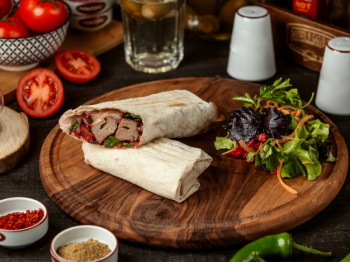 Side view of doner kebab wrapped in lavash with fresh salad on wooden board Free Photo