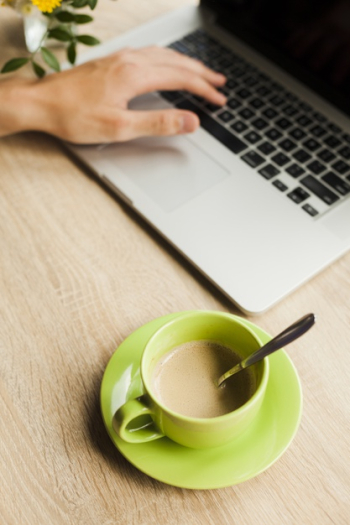 A person's hand using laptop with cup of coffee on wooden desk Free Photo