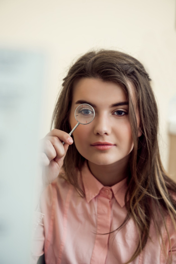 Horizontal portrait of good-looking focused woman on appointment with ophthalmologist holding lense and looking through it while trying to read word chart to check vision. eyecare and health concept Free Photo