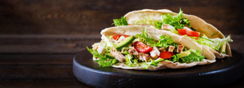 Pita bread sandwiches with grilled chicken meat, avocado, tomato, cucumber and lettuce served on wooden table Free Photo