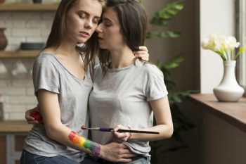Loving lesbian young couple with paintbrush and painted rainbow flag on hand Free Photo