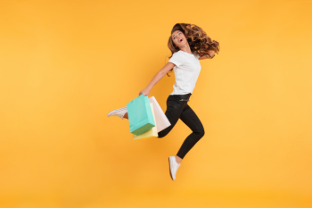 Laughing pretty young woman jumping holding shopping bags. Free Photo