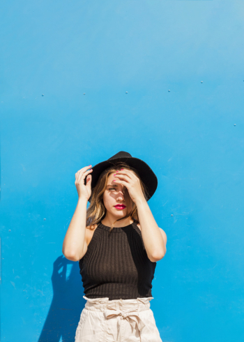 Stylish young woman with black hat standing in front of blue background