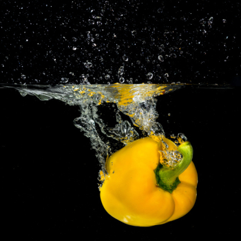 Fresh yellow bell pepper falling into the water with a splash and air bubble