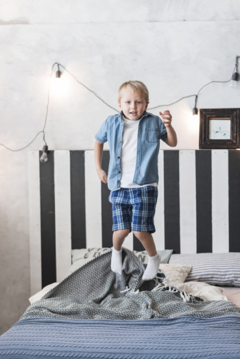 Portrait of a boy jumping over bed with decorated illuminated light on wall
