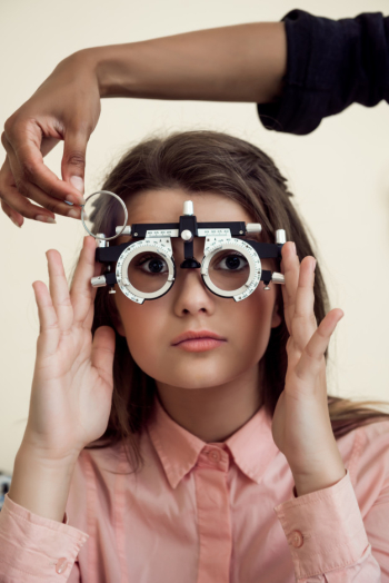 Horizontal shot of interested and curious caucasian girl on appointment with eye care specialist wearing phoropter while ophthalmologist checking her vision, sitting over yellow wall Free Photo