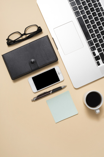 Cropped image laptop with eyeglasses; mobile phone; coffee cup and diary on beige background