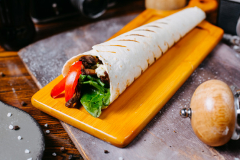 Side view of doner kebab wrapped in lavash on wooden board Free Photo