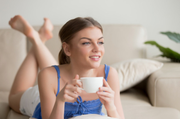 Dreamy woman relaxing on comfortable sofa, enjoying cup of coffe
