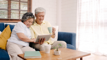Asian elderly couple using tablet and drinking coffee in living room at home, couple enjoy love moment while lying on sofa when relaxed at home. Free Photo