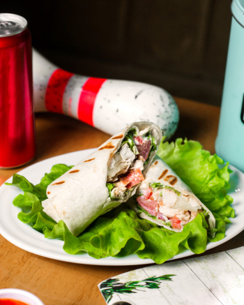 Side view of chicken doner wrapped in lavash on lettuce on wooden table Free Photo