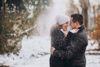 Young couple in winter under the snow falling from the tree Free Photo