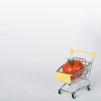 Fresh red tomato in shopping cart on white surface
