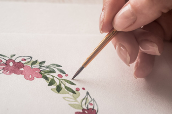 Young artist drawing flowers pattern with watercolor paint and brush on paper at workplace Free Photo