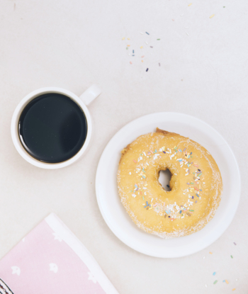 Cup of black coffee; whole donut and napkin on white backdrop