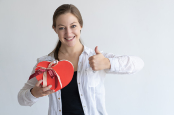 Happy lady showing heart shaped gift box and thumb up