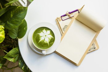 An overhead view of hot matcha green tea latte cup with clipboards on white table