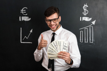 Close-up portrait of young smiling businessman holding bunch of money while showing thumb up gesture Free Photo