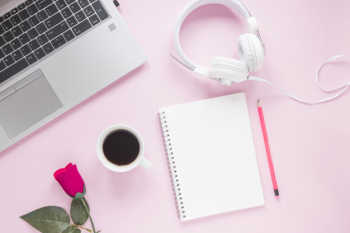 Rose; coffee cup; headphone; laptop; spiral notepad and pencil on pink background