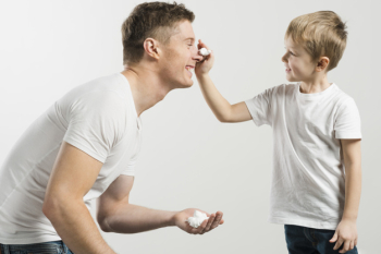 Father and son playing with shaving foam against white background