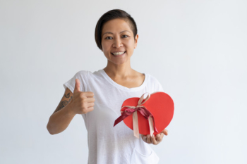 Smiling woman showing heart shaped gift box and thumb up