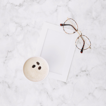 An overhead view of disposable coffee cup; empty frame and eyeglasses on marble textured background