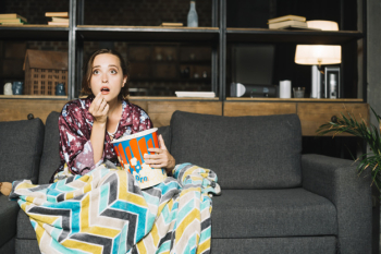 Shocked woman sitting on sofa with popcorn watching television