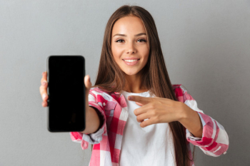Young pretty smiling woman pointing with finger on phone screen Free Photo