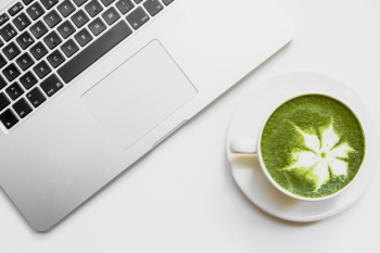 Japanese green tea latte in white cup near the laptop on white desk