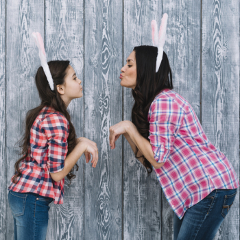 Side view of daughter and mother posing like a bunny pouting against gray wooden backdrop