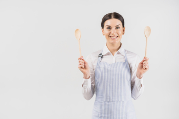 Female in apron smiling and holding spoons