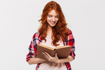 Smiling ginger woman in shirt holding and reading book Free Photo