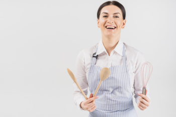 Woman in apron smiling and holding utensil