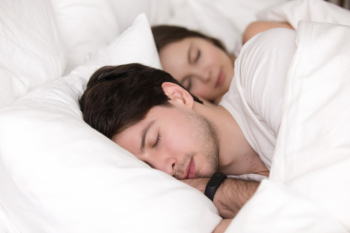 Sleeping young couple in bed, man wearing smart watch tracker