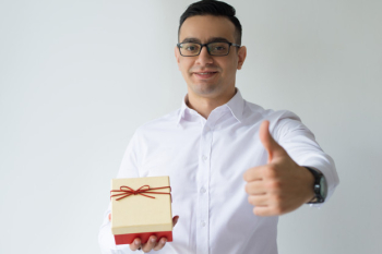 Smiling business man holding gift box and showing thumb up
