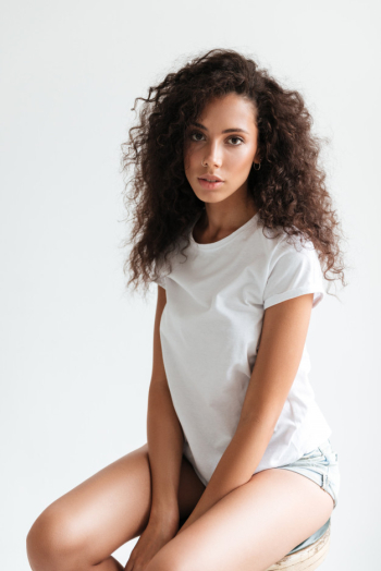 Beautiful young woman with curly hair posing while sitting Free Photo