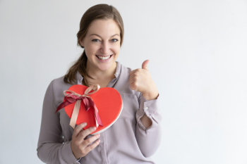 Cheerful lady showing heart shaped gift box and thumb up