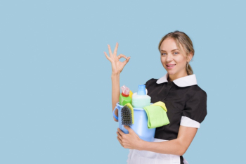 Young happy cleaner woman showing ok sign holding bucket of cleaning products over blue surface Free Photo
