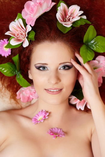 Closeup portrait of beautiful smiling redhead ginger woman face with colorful flowers in hair touching face Free Photo