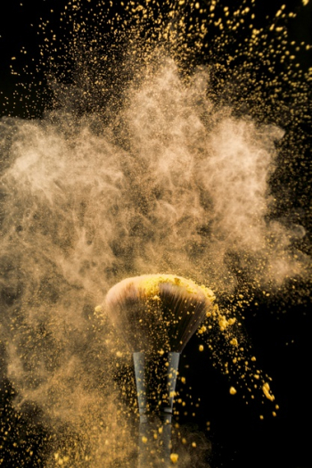Shaking cosmetic brush in yellow powder Free Photo