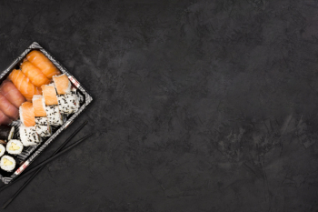 Sushi roll set on tray and chopsticks over dark textured surface with space for text