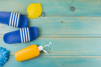 An overhead view of plastic yellow scallop; flip flops and sunscreen lotion bottle on turquoise wooden backdrop Free Photo
