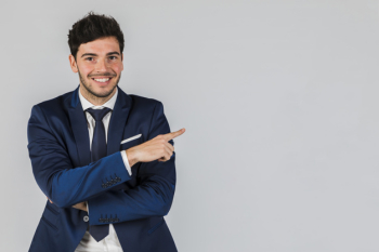 Portrait of a smiling young businessman pointing his finger against grey backdrop Free Photo