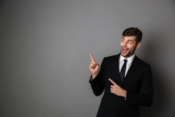Overjoyed brunette man in classic suit pointing with two fingers, looking aside Free Photo