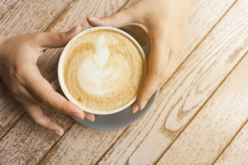 Top view of human hand holding latte coffee cup over wooden surface Free Photo