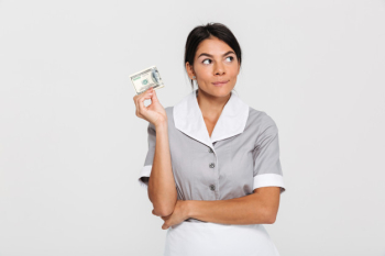 Close-up portrait of thinking pretty brunette woman in gray uniform holding dollar banknote and looking aside Free Photo
